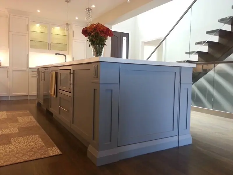 Renovated kitchen with grey island and marble top beside an open staircase